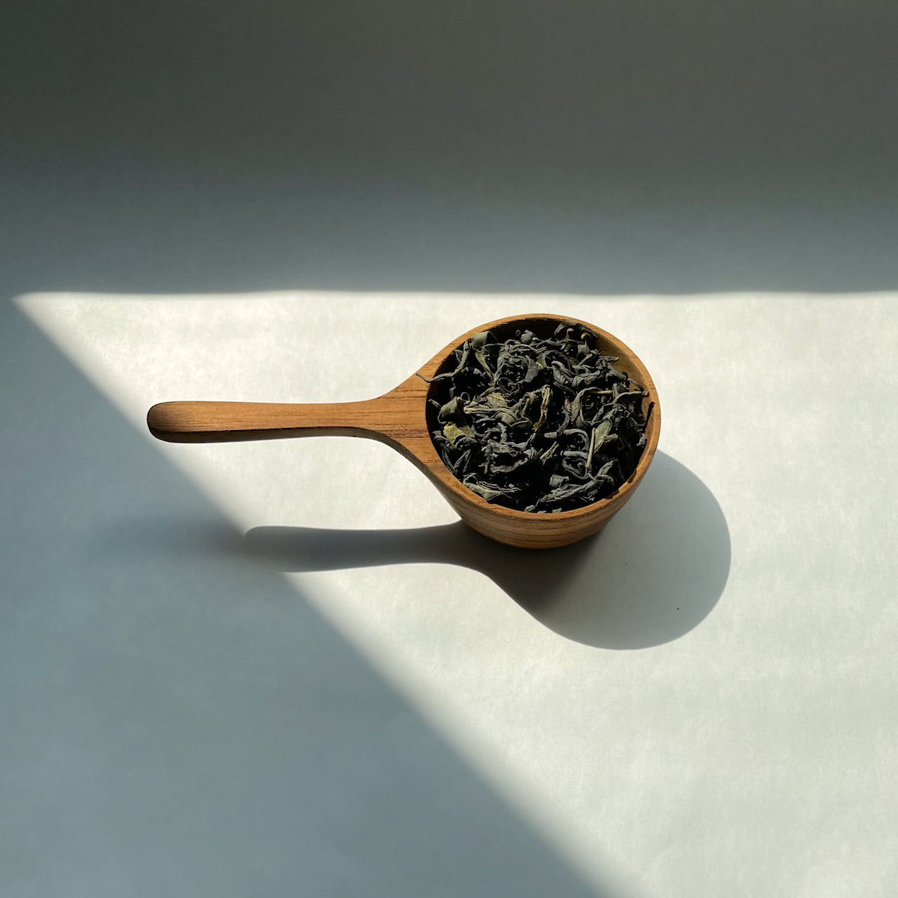 KINTO Tea Scoop offered by Wild rchid Tea, image of the wooden tea scoop with loose te leaves